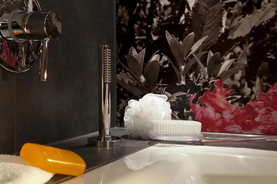 Badewanne mit Chromarmatur, Handbrause und dunkler Fliesenwand