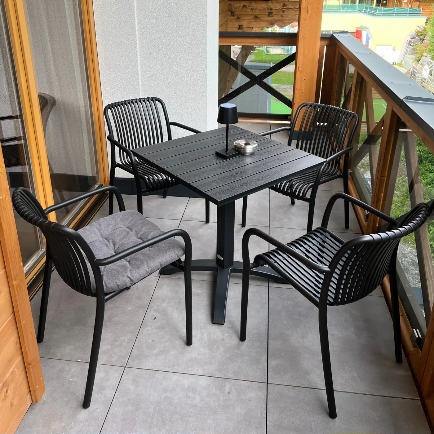 Überdachter Balkon mit schwarzem Tisch und vier Stühlen, Blick auf Wiese und Nachbarhäuser