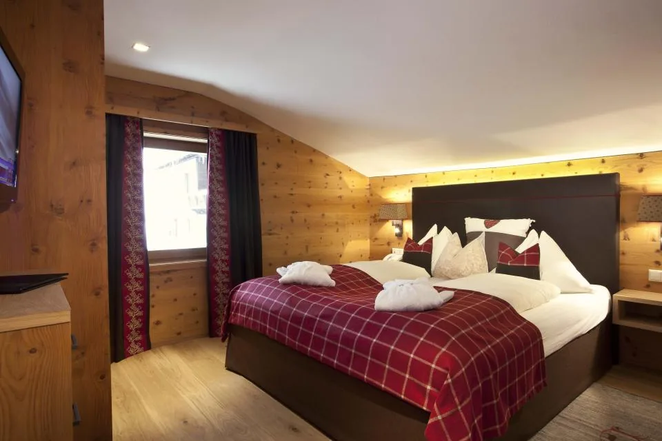 Zweites Schlafzimmer mit Zirbenholzwand, Doppelbett, roter Tagesdecke und Fernseher