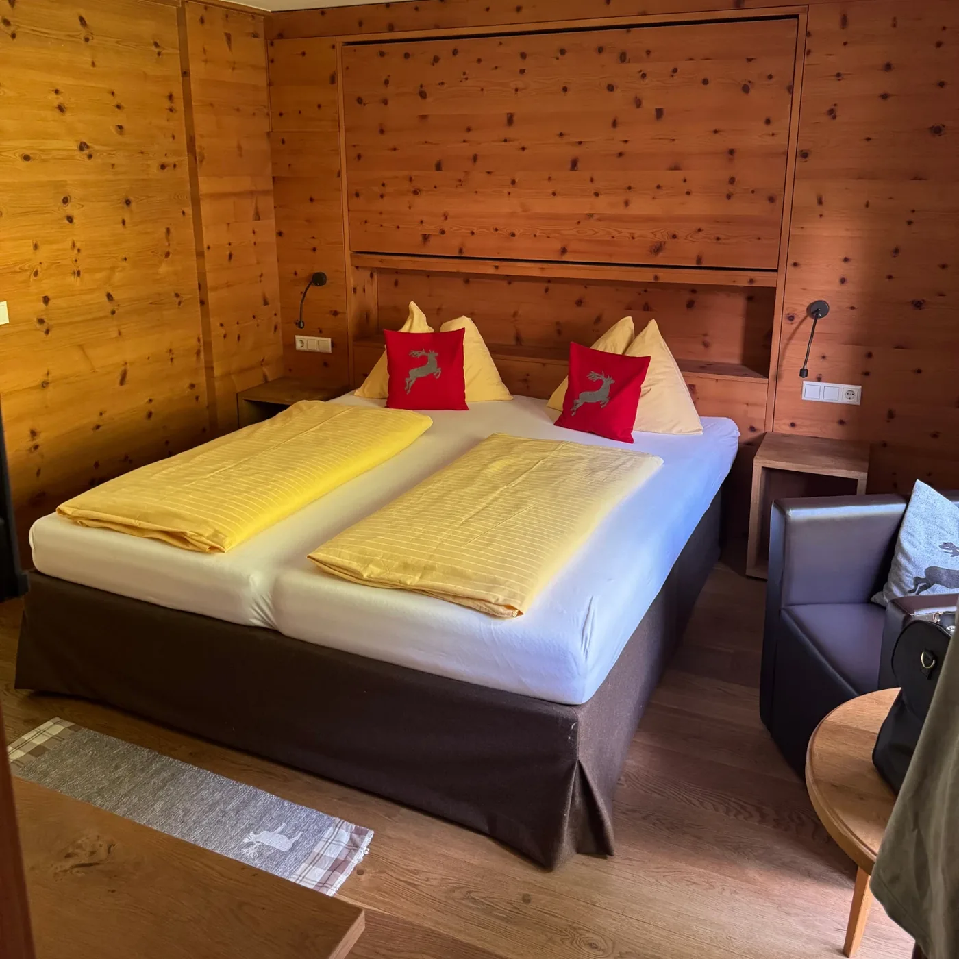 Schlafzimmer mit Wänden und Decke aus Zirbenholz, Doppelbett mit gelber Bettwäsche und roten Zierkissen