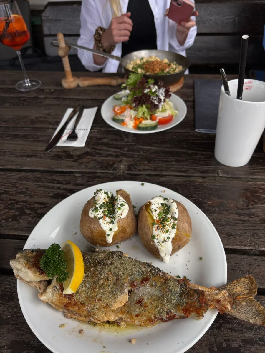 Gebratene Forelle mit Ofenkartoffeln und Sauerrahm auf einem rustikalen Holztisch