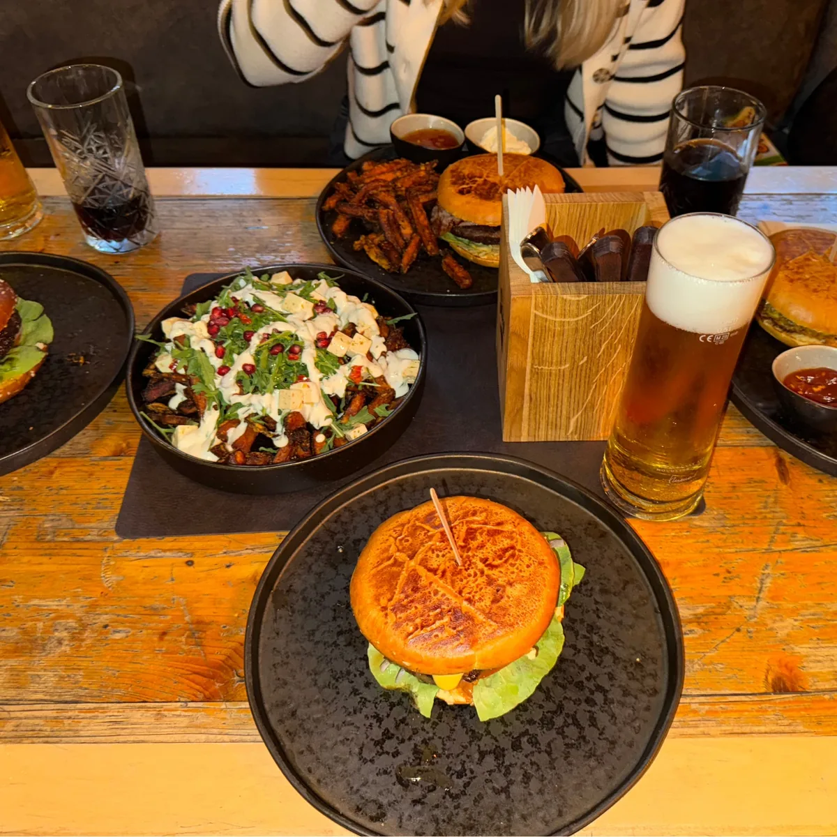 Burger mit Süßkartoffel-Pommes und einem Glas Bier auf einem Holztisch