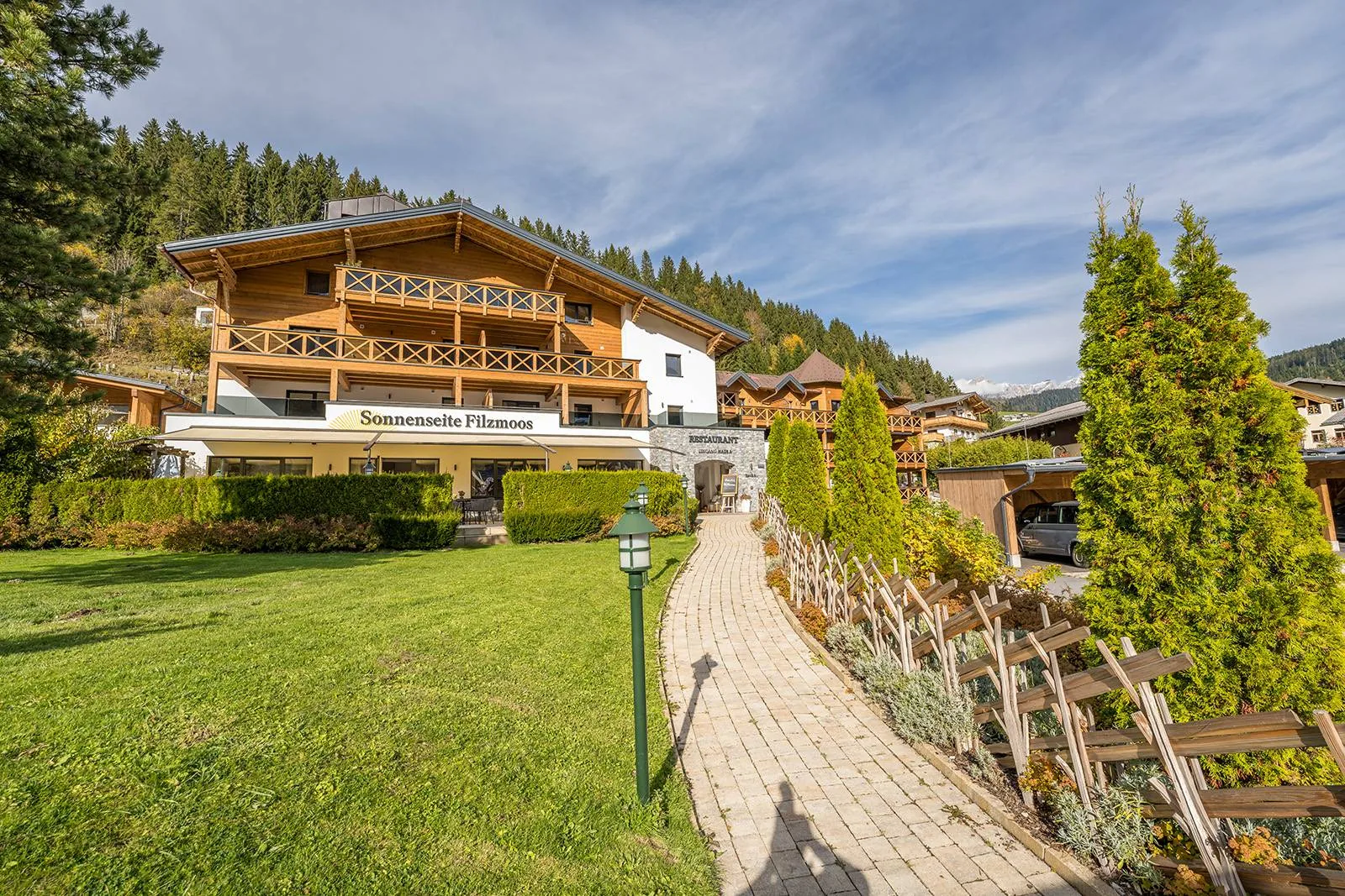 Das Haus Sonnenseite Filzmoos mit Holzbalkonen, davor eine Wiese und der Weg zum Eingang